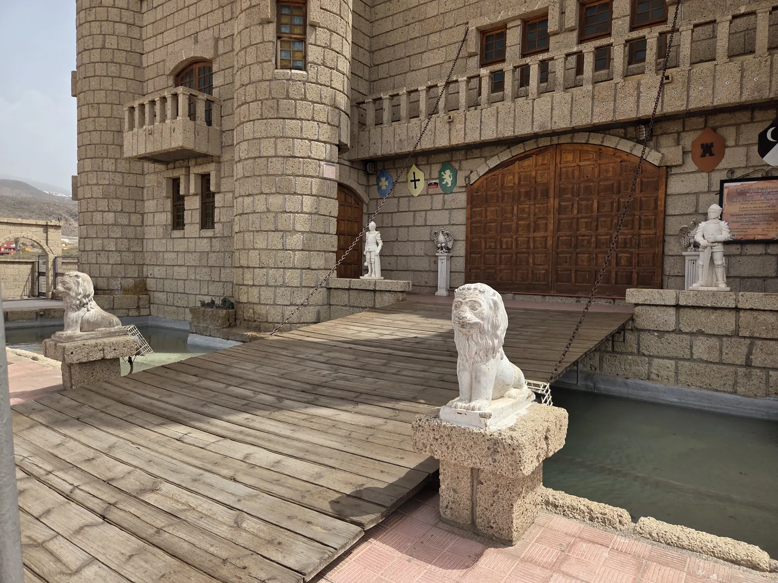Wooden entrance bridge at Castillo San Miguel with white lion statues, stone towers and a large wooden gate