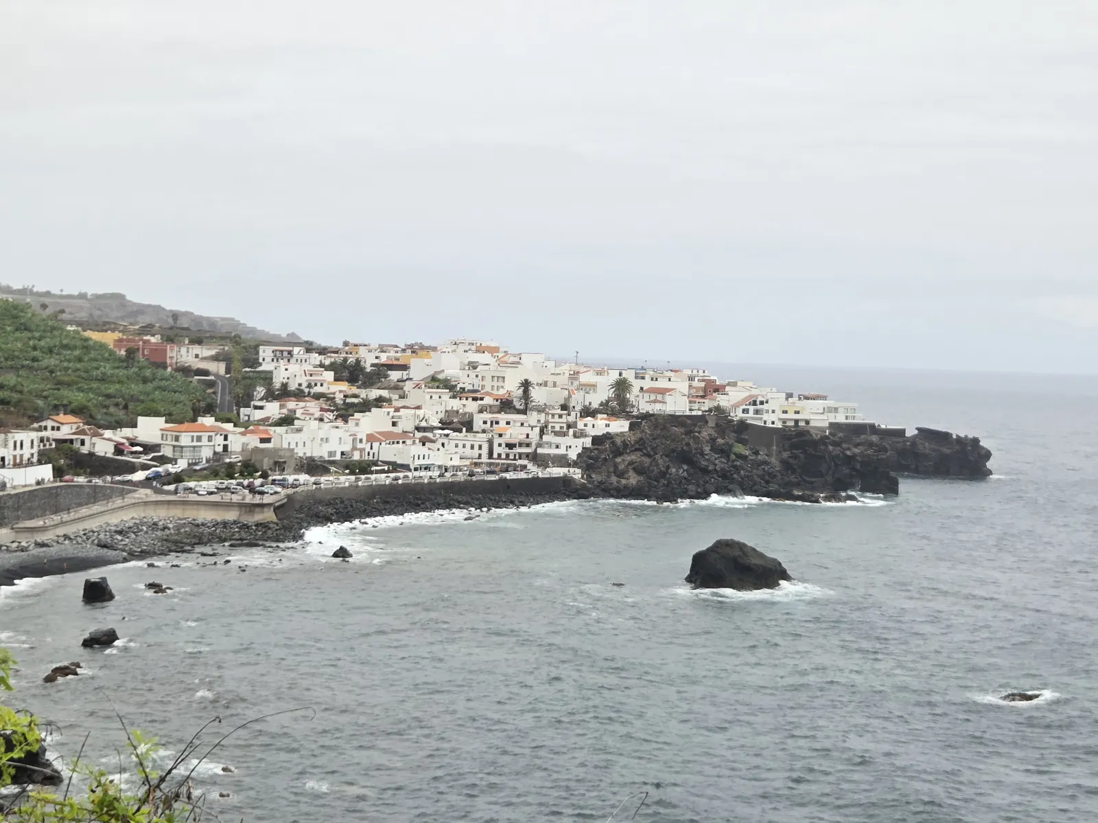 White buildings of Las Aguas above a rocky Atlantic shoreline with offshore rocks