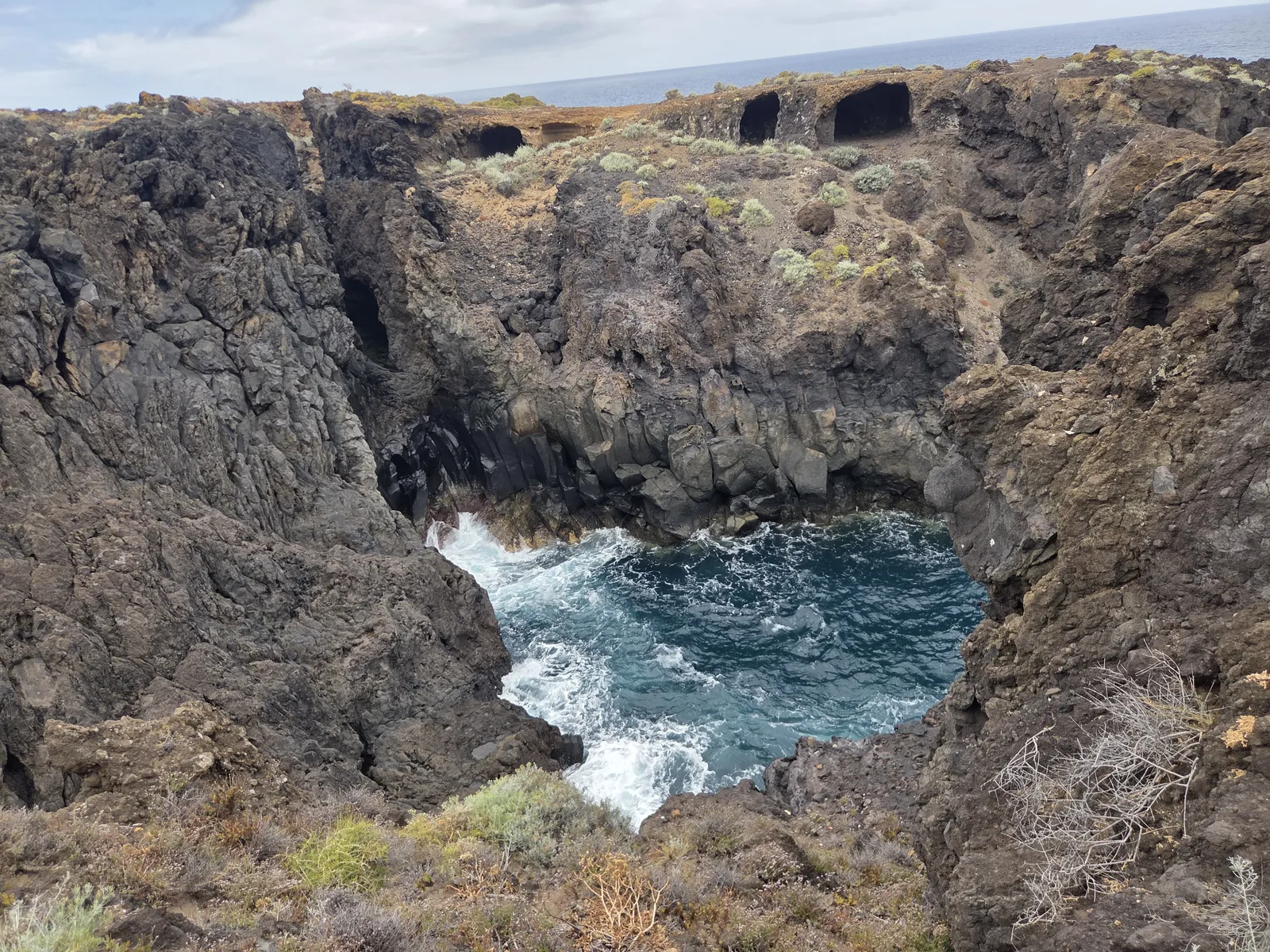 Atlantic water surging into a narrow inlet surrounded by dark fractured volcanic rock