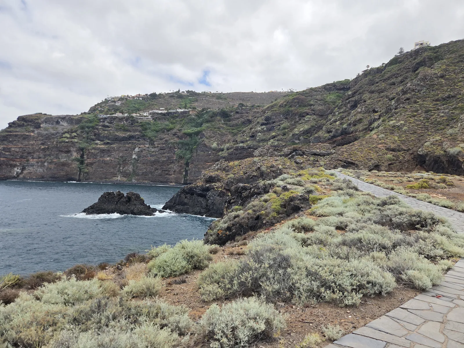 Coastal footpath through low scrub beside volcanic rocks and steep cliffs in El Sauzal