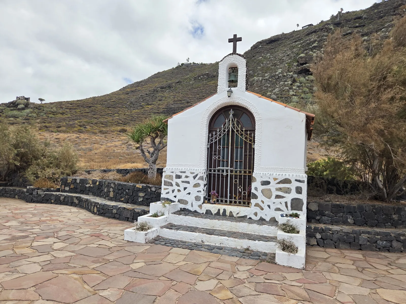 Whitewashed Ermita de Rojas with a bell, cross and gated arched entrance