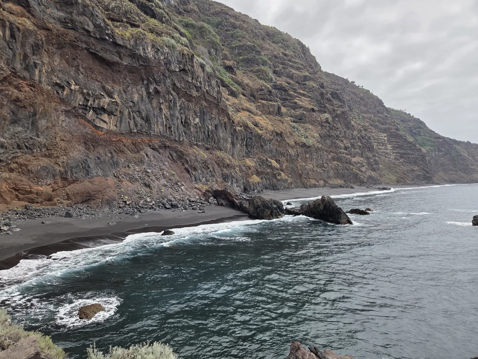 Dark volcanic cliffs above Garañona Beach, with offshore rocks and white Atlantic surf