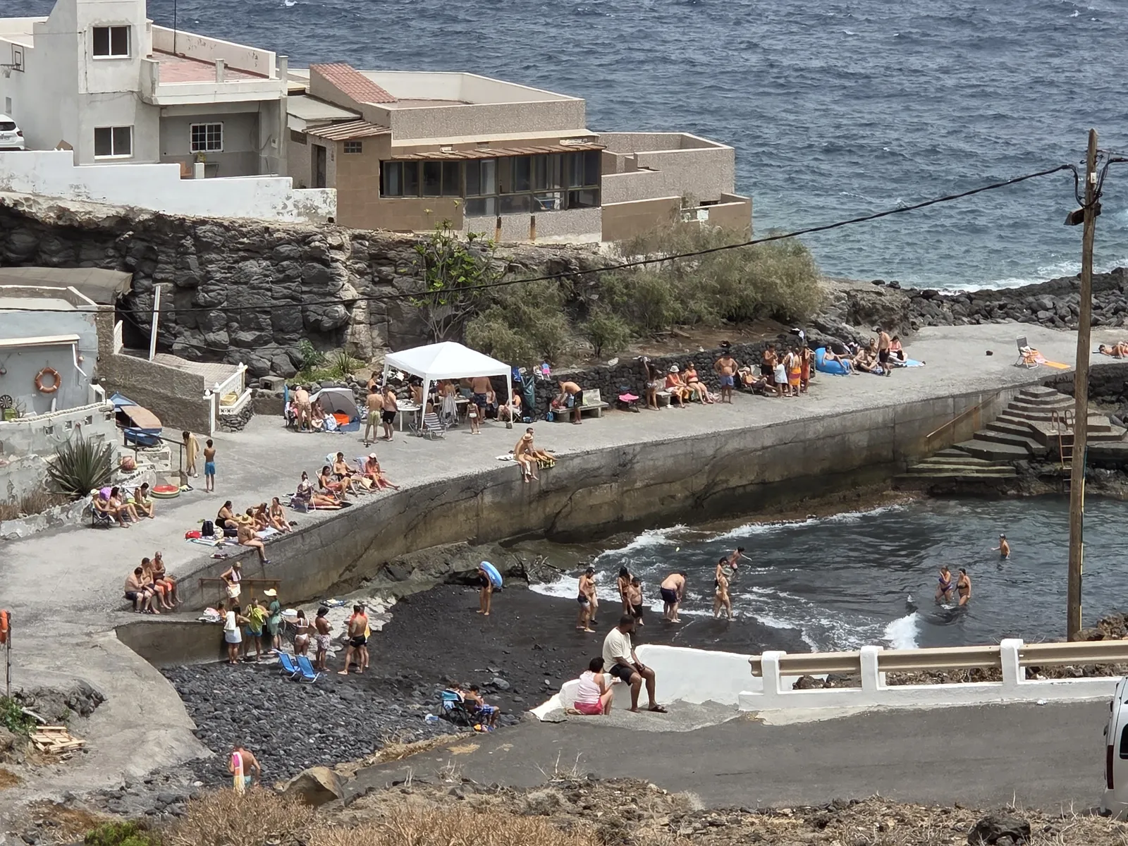 Bathers at La Caleta’s black-pebble cove beside a concrete waterfront platform and steps