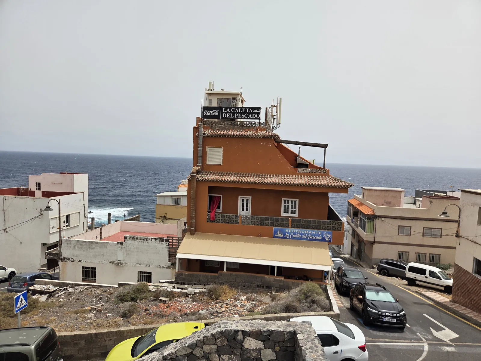 Ochre restaurant building with a La Caleta del Pescado rooftop sign and the Atlantic behind it