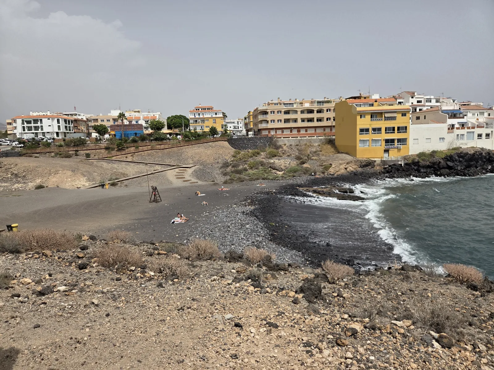 Dark sand and pebble beach beside the waterfront buildings of Los Abrigos