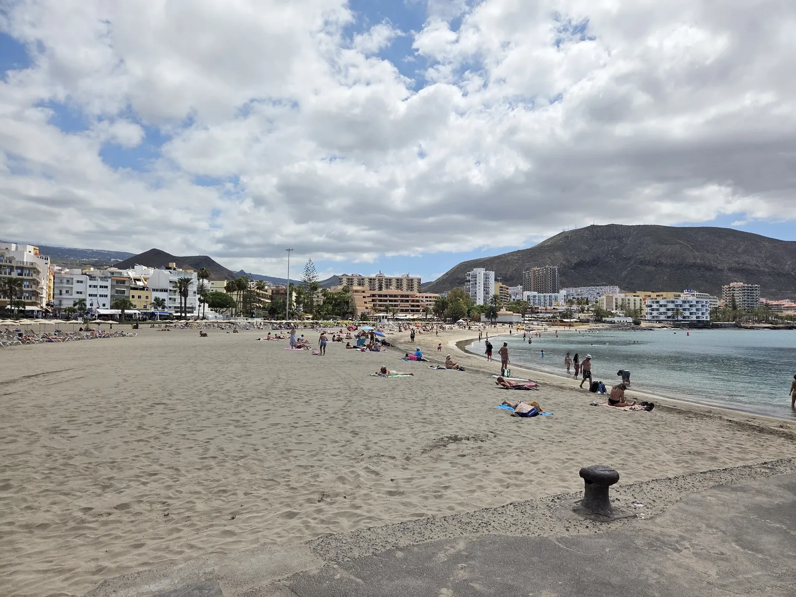 People sunbathing and swimming along the curved sandy shoreline of Playa de Los Cristianos