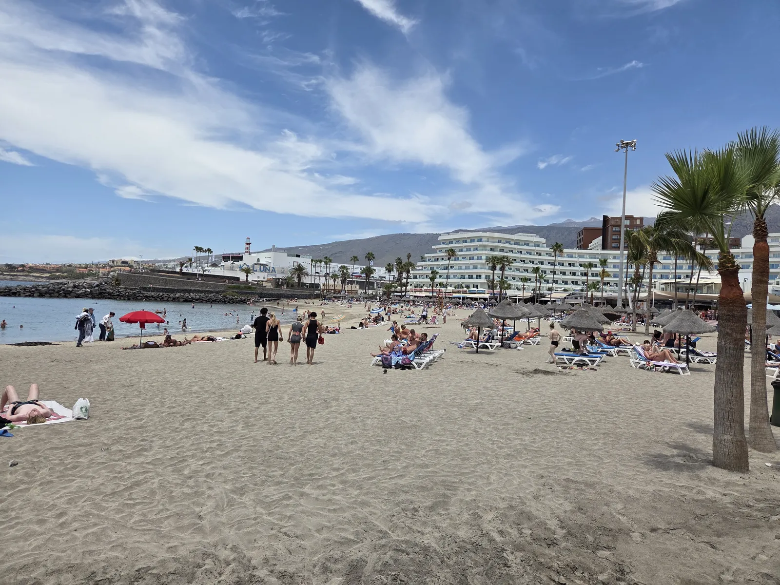 Sandy resort beach with swimmers, sun loungers, parasols and palm trees