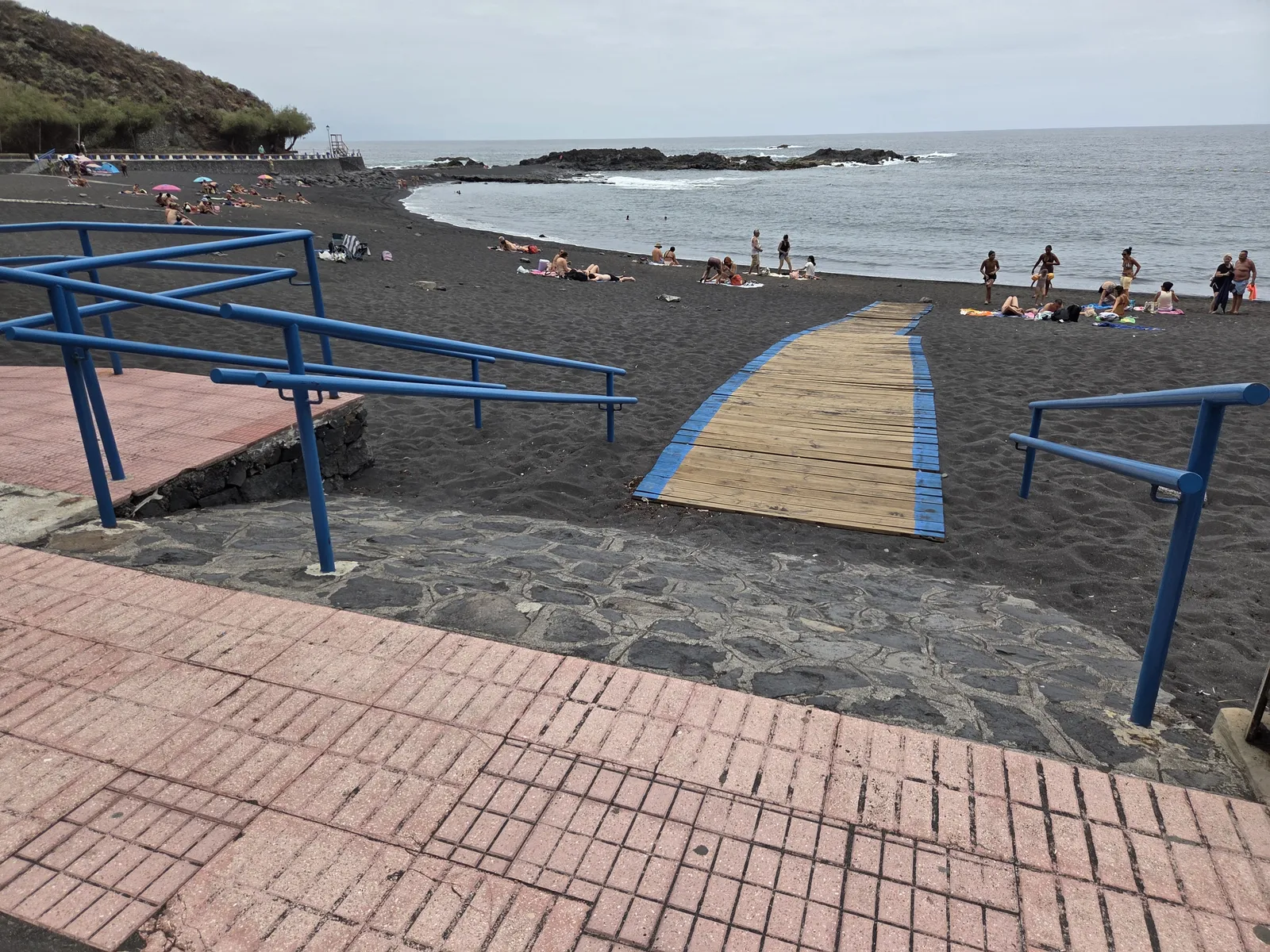 Blue handrails and a wooden walkway leading onto the black sand at Playa de la Arena