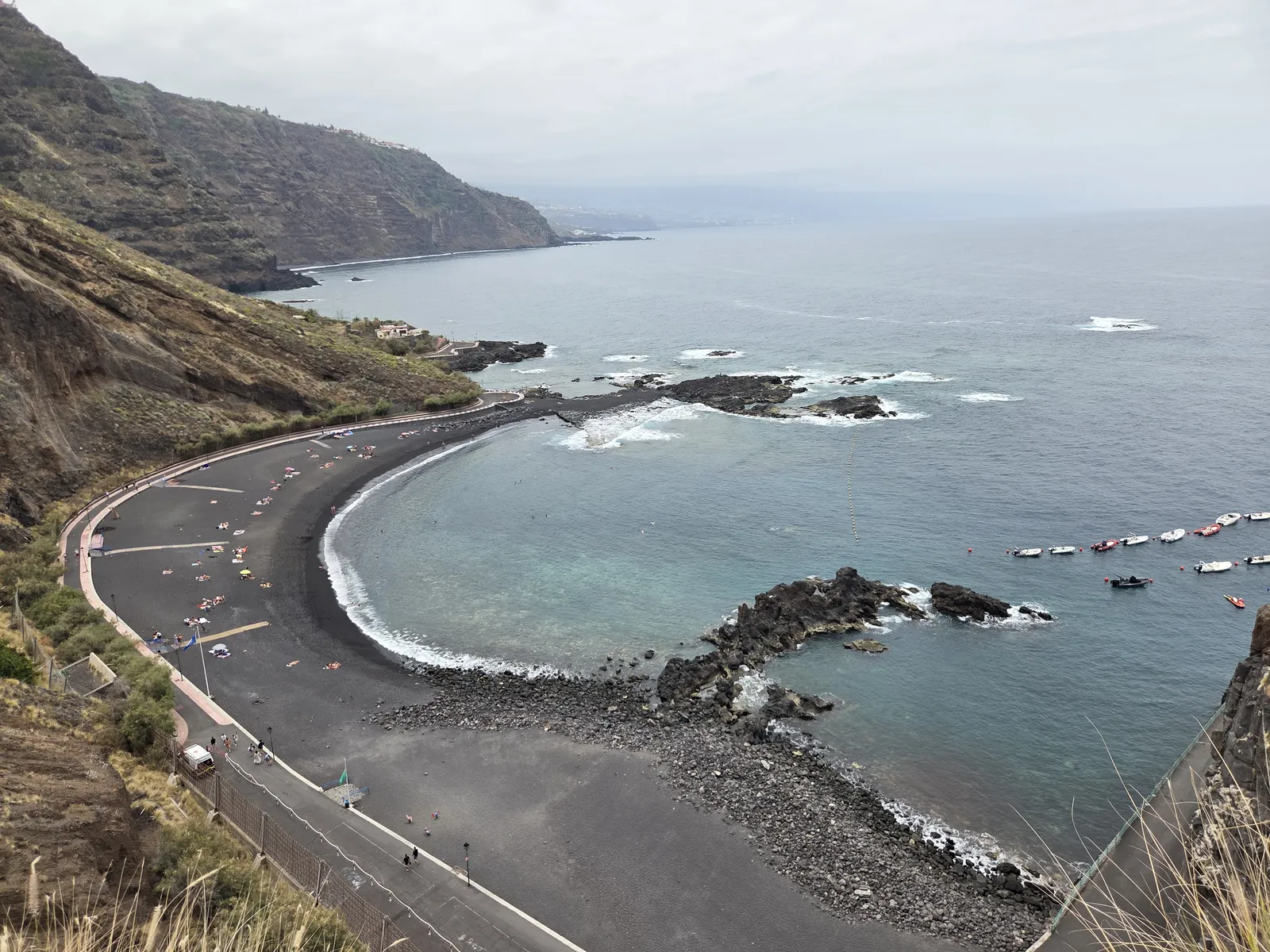 Curving black-sand beach at Mesa del Mar beneath steep cliffs, with volcanic rocks offshore