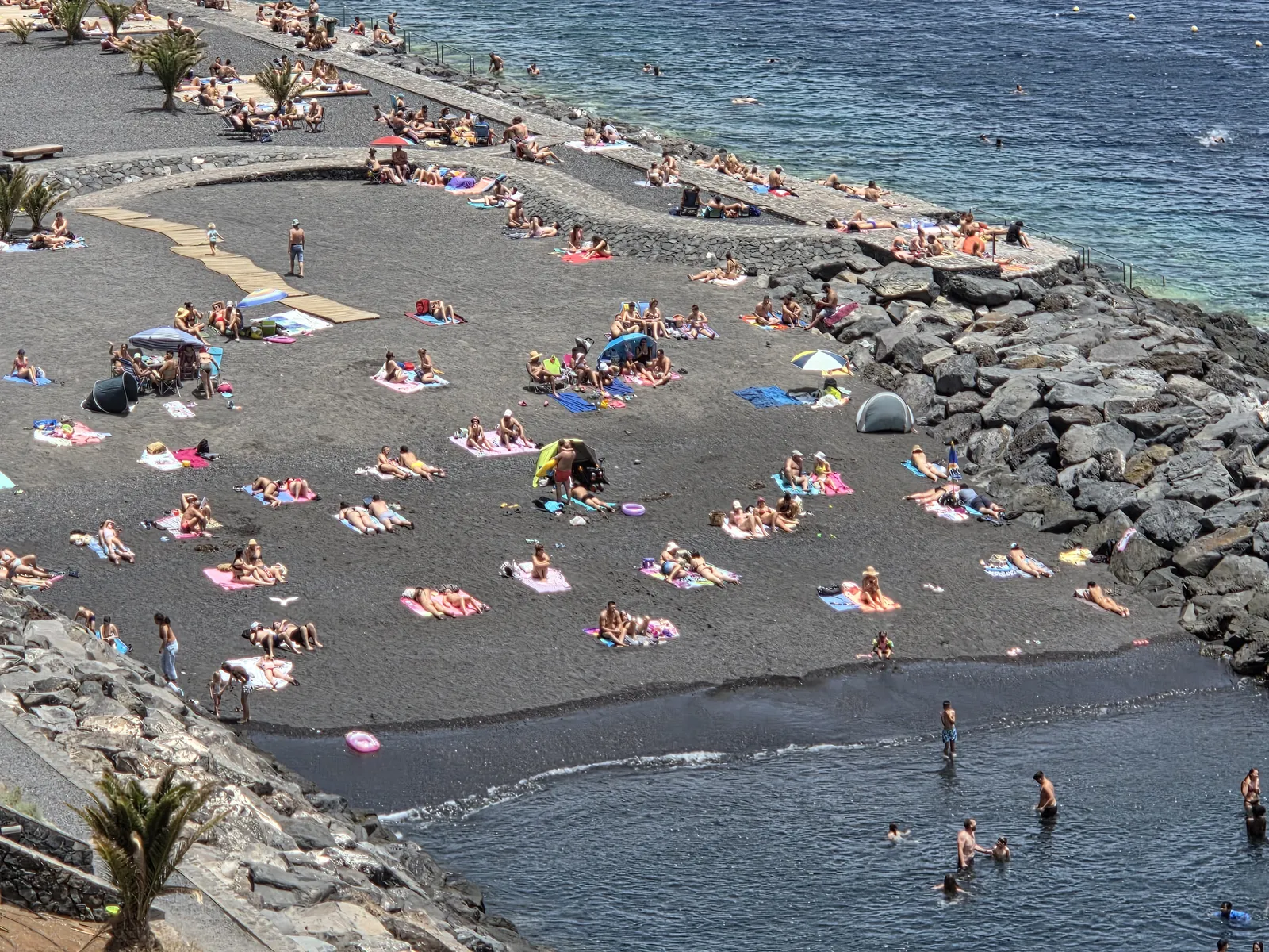 Bathers on small black-sand coves separated by rock barriers at Radazul