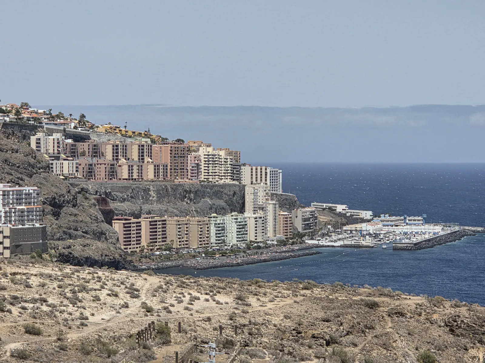 Apartment buildings above Radazul’s coastline and marina, with dry slopes in the foreground