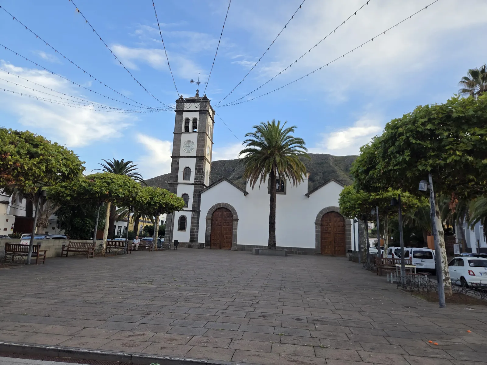 San Marcos church and its bell tower facing a paved square shaded by trees and palms