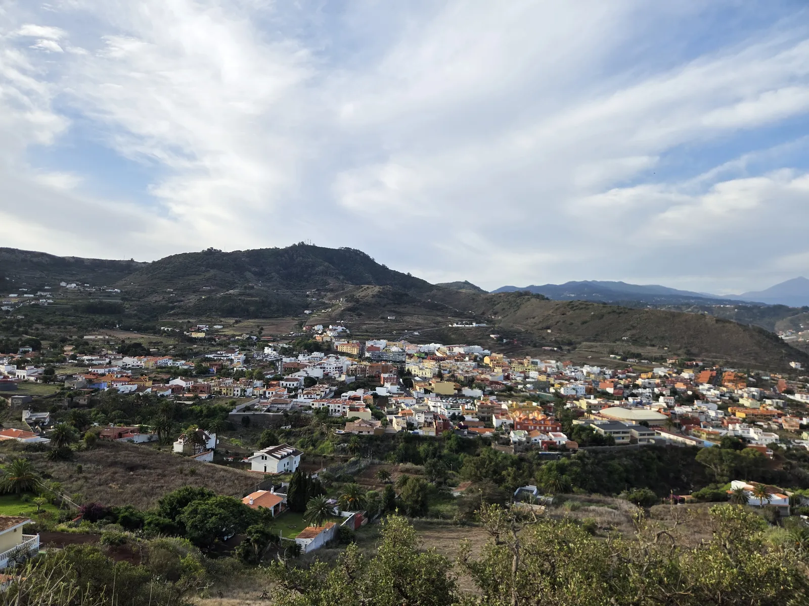 Tegueste spread across a green valley beneath rocky hills and a cloudy sky